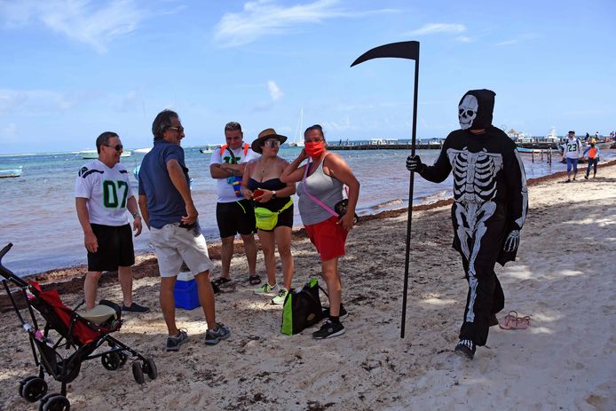 Een man verkleed als 'de dood’ waarschuwt toeristen in Puerto Morelos naaer huis te gaan, omdat de stranden gesloten zijn